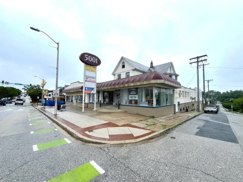 Corner view of commercial building at 5001-5003 Harford Road with red awnings and pole signage.