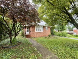 Front view of 5900 Winthrope Avenue, a brick bungalow in Baltimore’s Hamilton neighborhood with mature trees and concrete walkway.