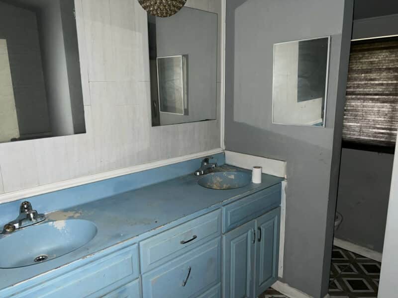 Full bathroom with blue dual-sink vanity, two mirrors, and gray walls.