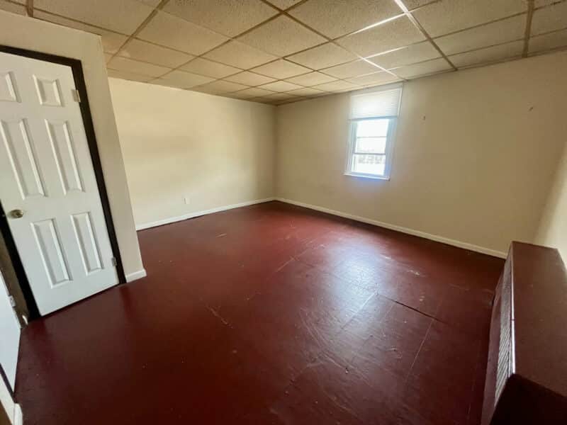Empty room in Apartment 2 at 4831 Belair Road with red painted floors, white walls, and ceiling tiles.