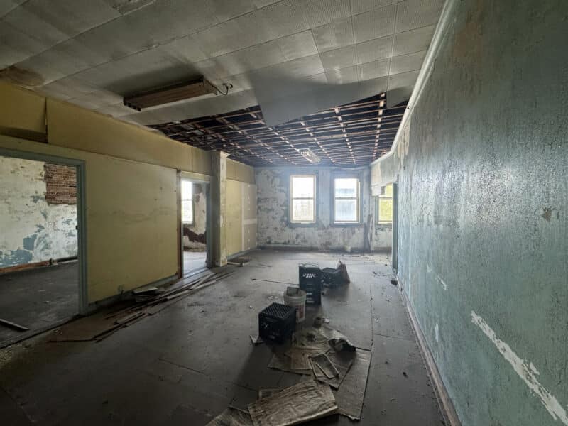 Second-floor room with exposed ceiling and large front-facing windows.