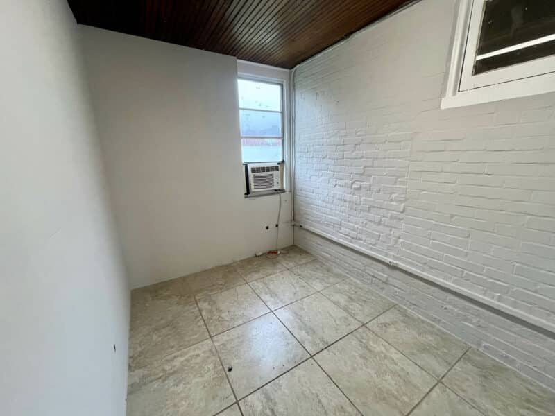 Small tiled room with window A/C unit and painted brick wall in rear second-floor unit at 5839 Belair Road.