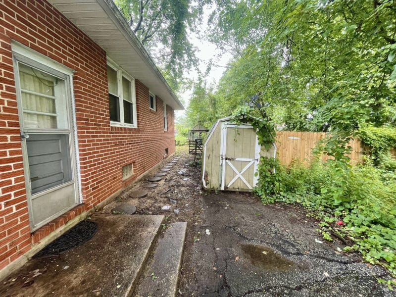 Rear side walkway of 5900 Winthrope Avenue with brick exterior, fenced yard, and utility shed.