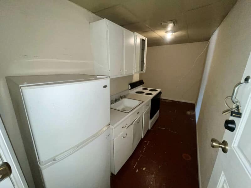 Galley-style kitchen in Apartment 2 at 4831 Belair Road featuring white cabinets, appliances, and red painted flooring.