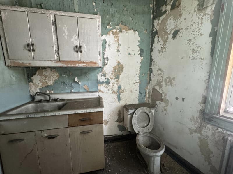 Bathroom with aged vanity and exposed plumbing in need of full renovation.