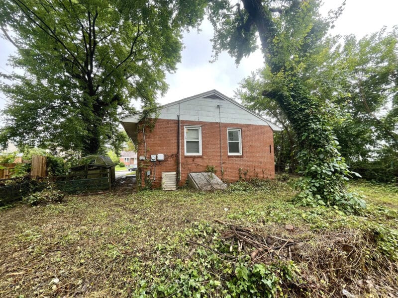 Rear exterior of brick bungalow at 5900 Winthrope Avenue with two small windows, utility meters, and cleared yard space.
