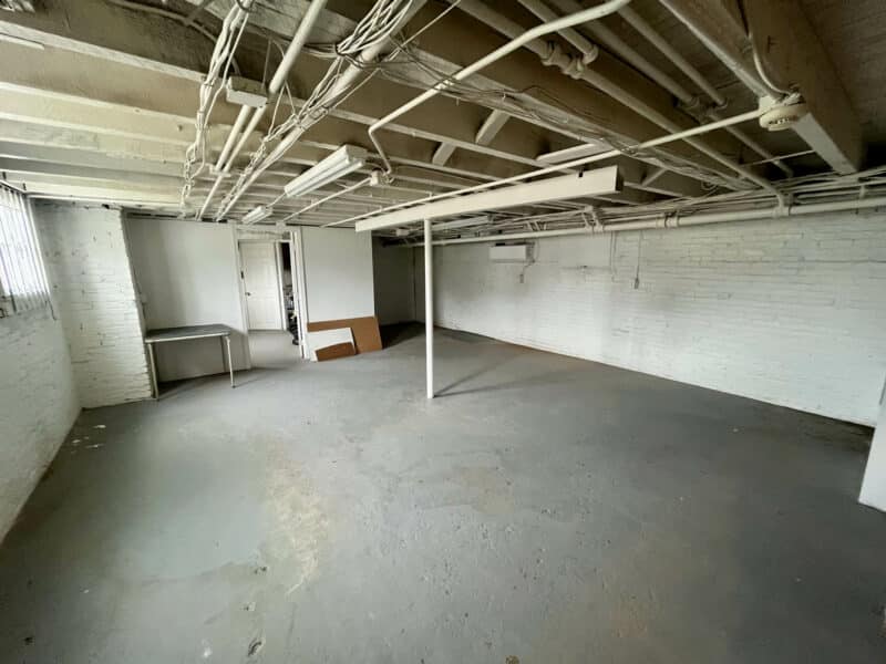 First basement room at 5839 Belair Road with exposed ceilings, painted brick walls, and concrete flooring.