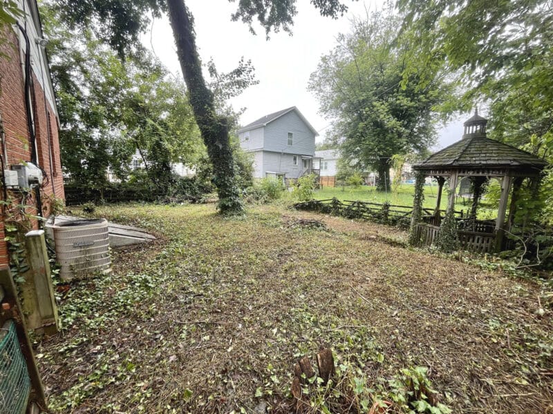 Backyard view of 5900 Winthrope Avenue with open lot, mature trees, and wooden gazebo.