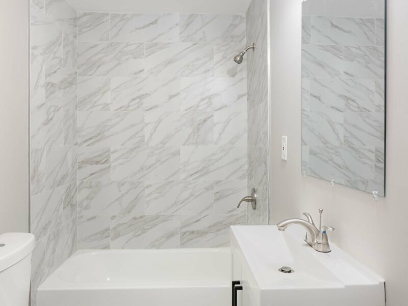 Updated bathroom at 5248 Cordelia Avenue featuring white vanity, modern faucet, and marble-style tile tub surround.