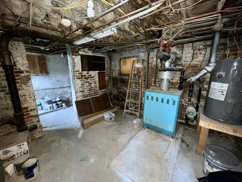 Basement mechanical room with boiler, water heater, exposed brick walls, and utility connections at 5839 Belair Road.