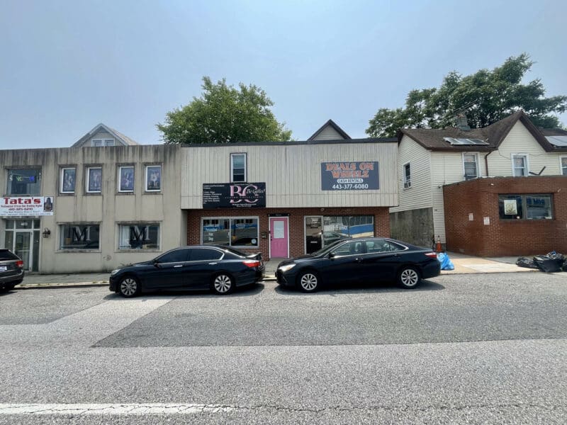 Wide-angle view of 4831 Belair Road showing full building frontage with retail storefronts, neighboring properties, and street parking in Baltimore.