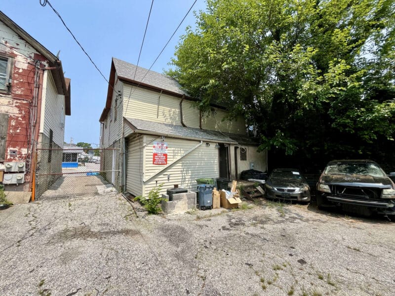 Rear exterior of 4831 Belair Road showing fenced parking lot, alley access, and rear entrances to commercial building.