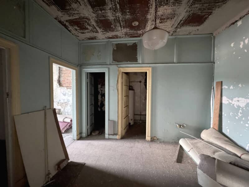 Interior view of a room with blue walls, distressed ceiling, and multiple doorways leading to adjacent spaces.