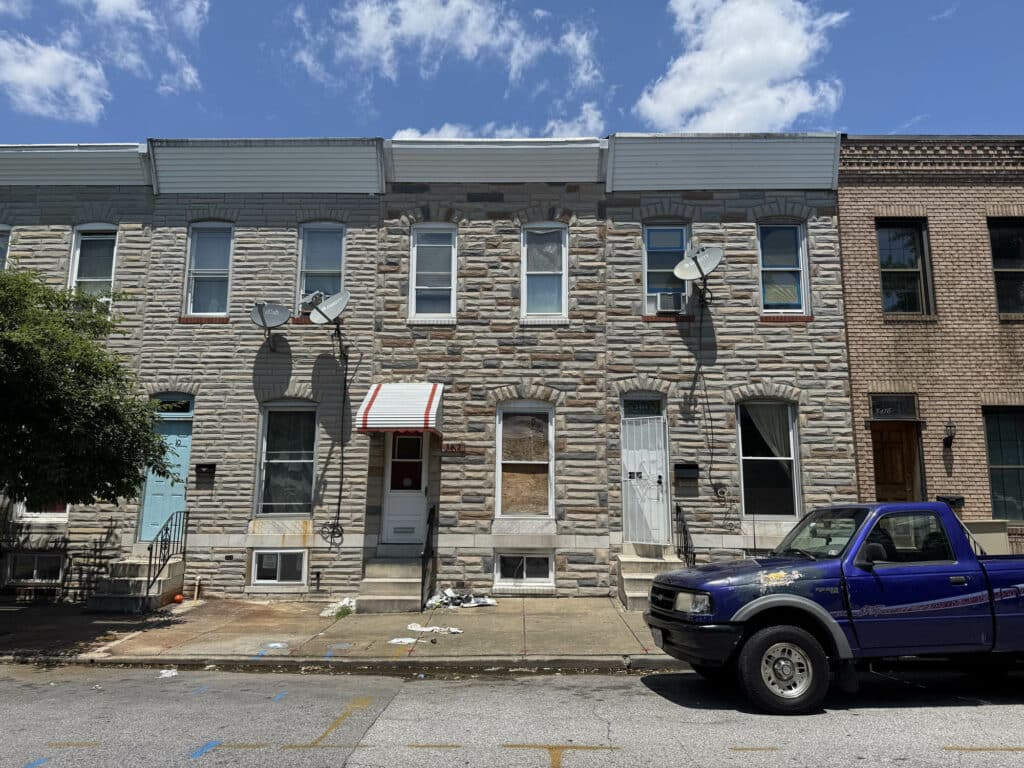 Front exterior of two-story brick townhome with stone facade, red-and-white awning, and adjacent parked car on Esther Place in Highlandtown area, Baltimore City.