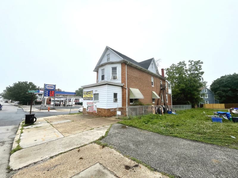 Street corner view of 5839 Belair Road showing commercial building, sidewalk, signage, and adjacent green space.