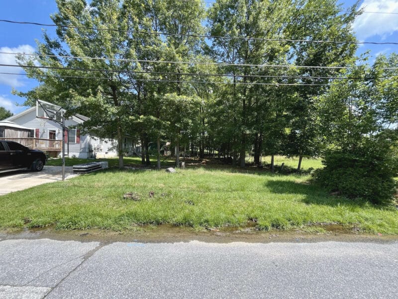 Street-level view of 4812 Valley Forge Road in Randallstown, Maryland, showing a grassy and partially wooded residential lot.