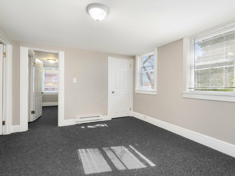 View of first bedroom with neutral carpet, fresh paint, and double windows in Baltimore City bungalow.