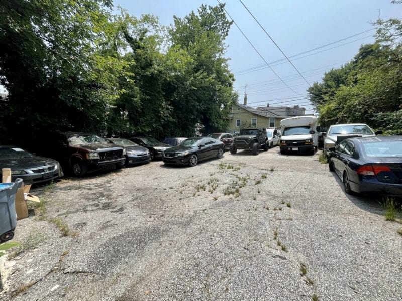 Large fenced parking lot behind 4831 Belair Road with multiple vehicles and alleyway access.