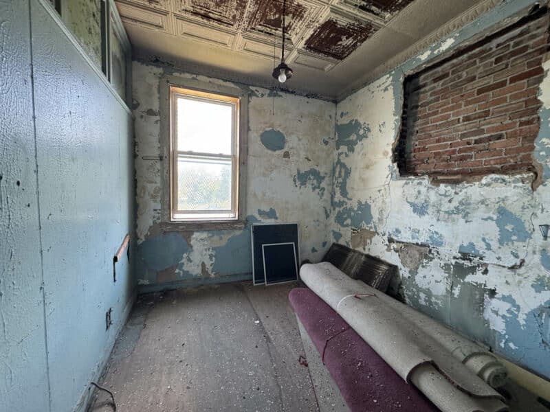 Small upper-level room with distressed plaster walls, exposed brick, and rolled carpet on the floor.