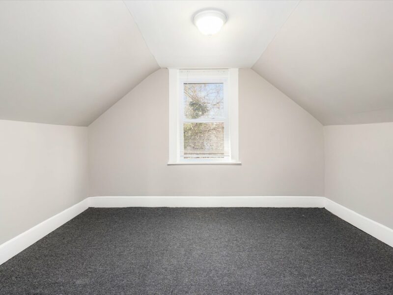 Second-floor bedroom with sloped ceilings, neutral walls, and fresh carpeting in a renovated Baltimore bungalow.