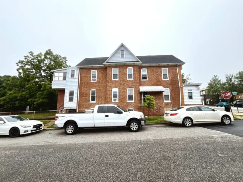 Side street view of 5839 Belair Road with two and one-half story brick building and parked vehicles in front.