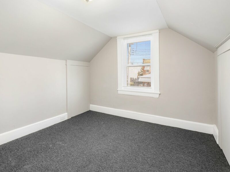 Second-floor bedroom with sloped ceilings, neutral walls, and fresh carpeting in a renovated Baltimore bungalow.
