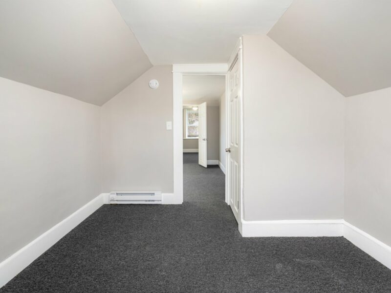 Upper-level third bedroom with neutral walls, sloped ceilings, and fresh carpet in a renovated Arlington bungalow.
