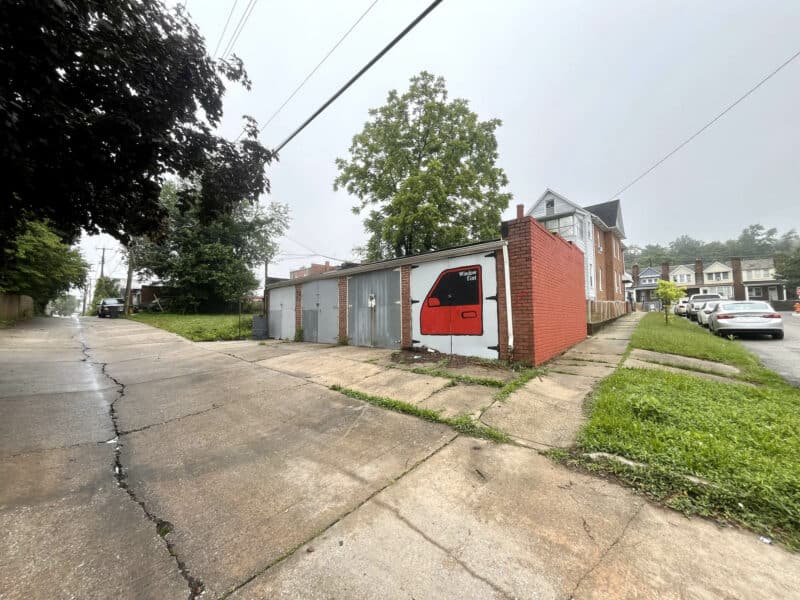 Rear alley view of four-door brick garage at 5839 Belair Road, including driveway and painted mural.