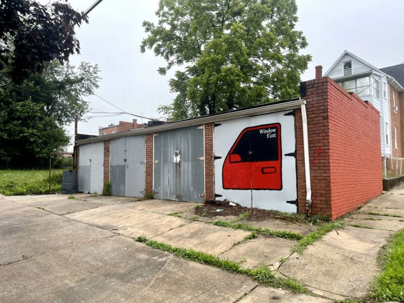Close-up of four-unit brick garage with metal doors and vehicle mural at 5839 Belair Road.