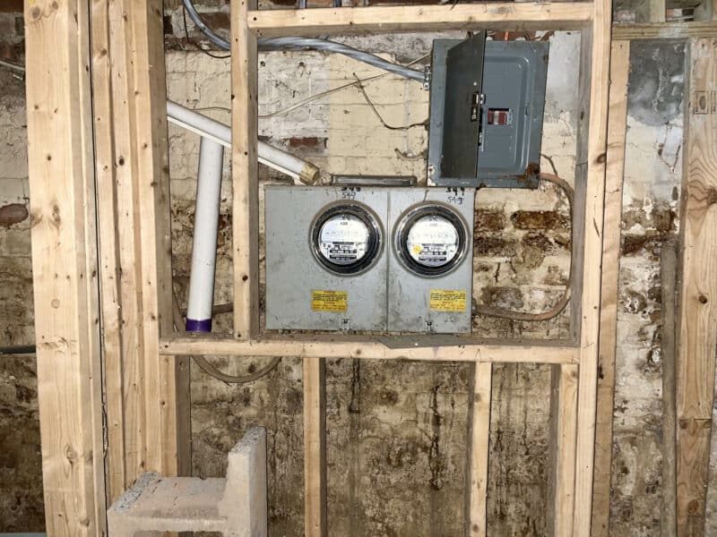 Dual electric meters and panel mounted on unfinished framed wall