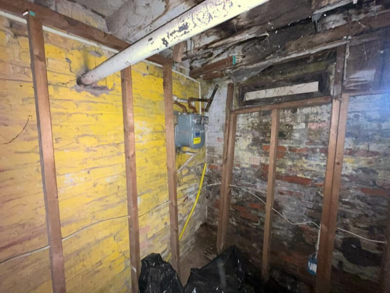 Basement framing with exposed brick, yellow insulation, and gas line