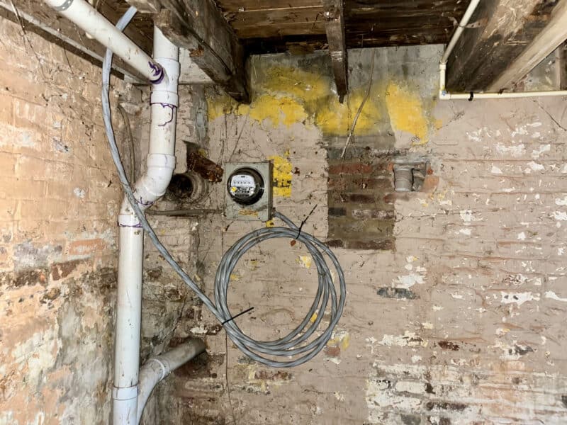 Exposed brick basement wall with utility meter, wiring coil, and white PVC plumbing