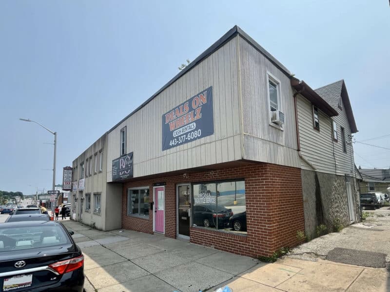 Angled exterior view of 4831 Belair Road showing sidewalk frontage, corner exposure, retail signage, and side alley access in Baltimore City.