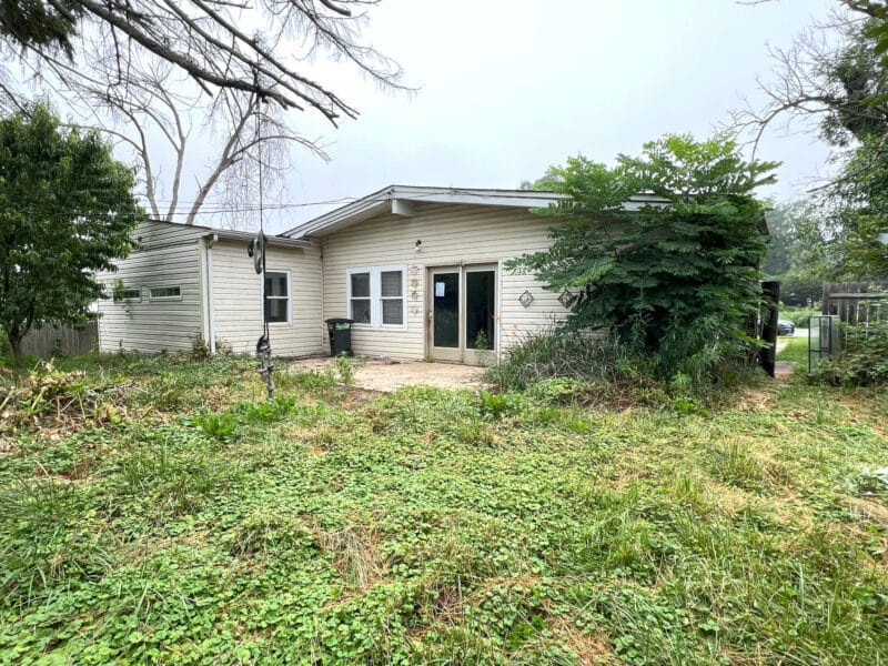 Back view of split-level home at 4761 Bonnie Brae Road with overgrown yard, rear entrance, and concrete patio.