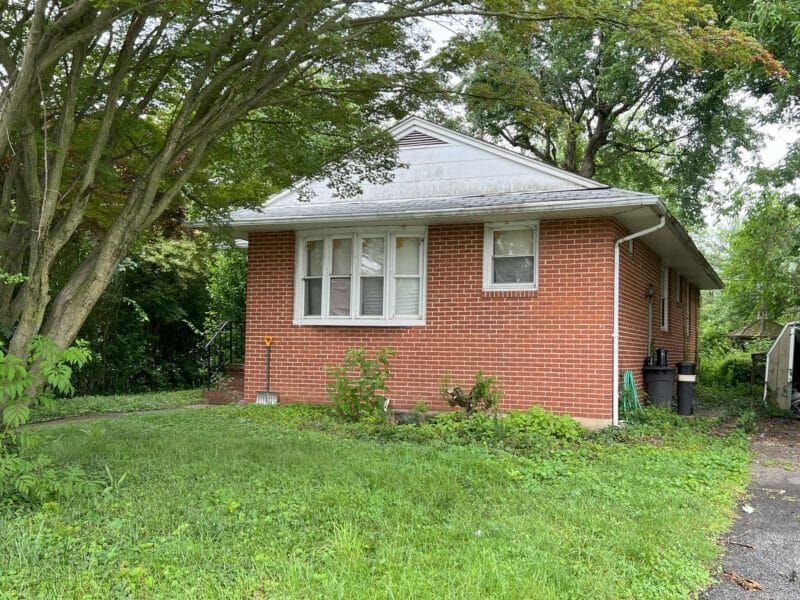 Front view of 5900 Winthrope Avenue, a brick bungalow in Baltimore’s Hamilton neighborhood with mature trees and concrete walkway.