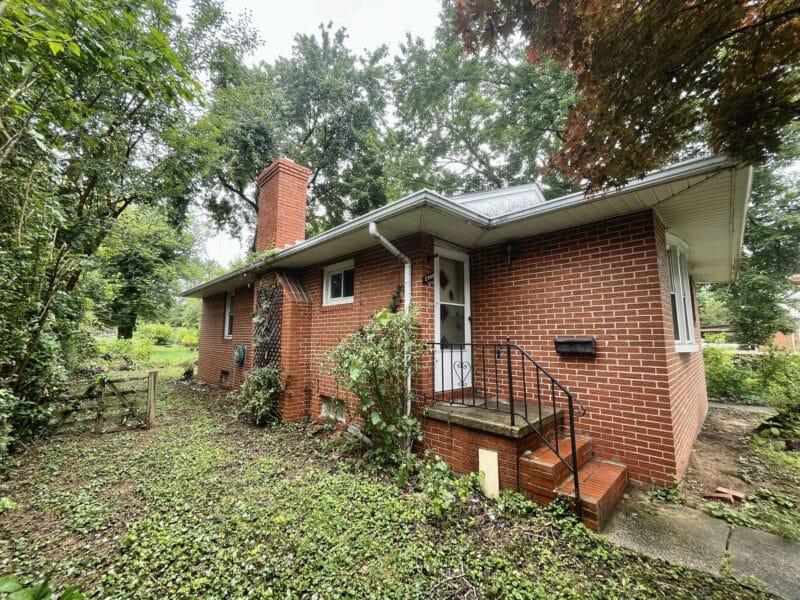 Front view of 5900 Winthrope Avenue, a brick bungalow in Baltimore’s Hamilton neighborhood with mature trees and concrete walkway.