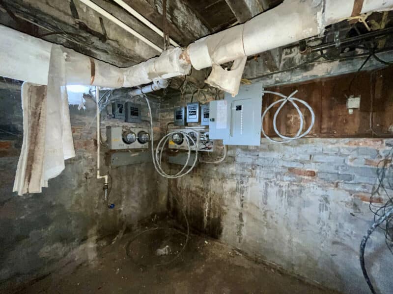 Basement electrical panel area with meters, conduit, and exposed brick walls
