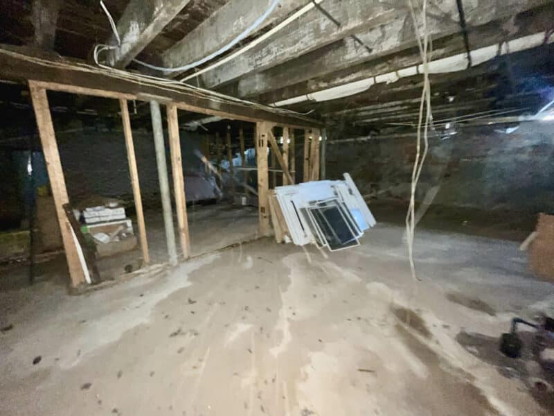 Unfinished basement area with concrete floor, exposed beams, and stored construction materials