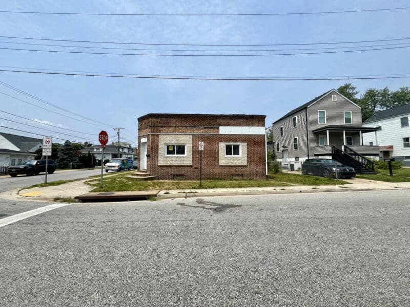 Street view of a corner brick building with flat roof and two windows on front
