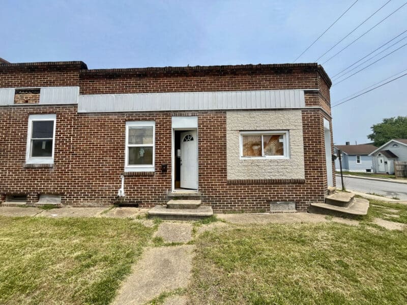 Front elevation of a one-story brick building with white door and three front-facing windows