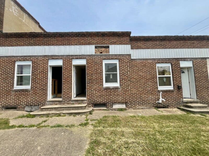 Brick facade of a one-story building with three separate entrances and concrete steps