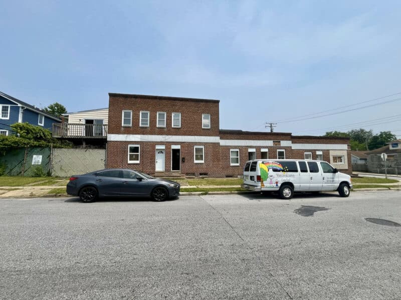 Wide-angle street view of a multi-unit brick building with vehicles parked out front