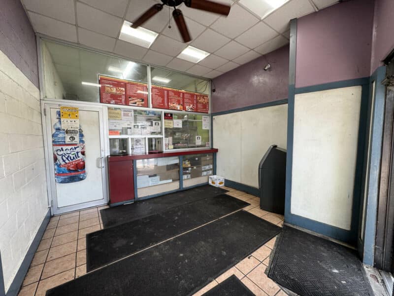Interior view of restaurant storefront at 5109 Park Heights Avenue showing order counter with menu board, protective glass, and tile flooring.
