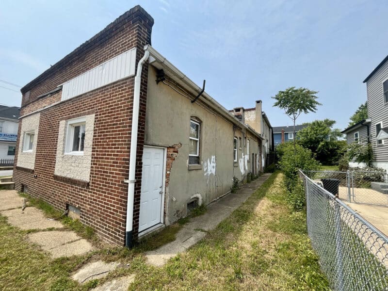 Side and rear exterior view of a brick multi-unit building with gated yard access
