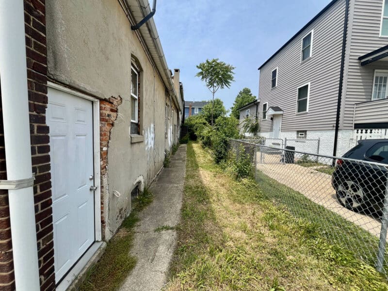 Narrow walkway and grassy rear access path alongside multi-unit building
