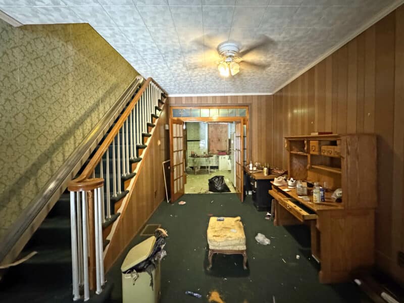 Dining room interior of 3412 Esther Place featuring wood-paneled walls, stairway with banister, vintage light fixture, and visible clutter, highlighting renovation potential.