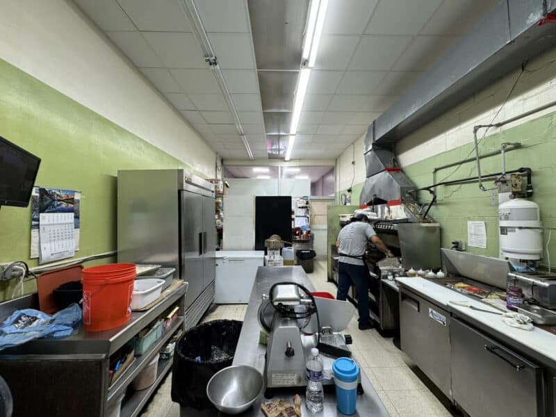 Commercial kitchen with stainless steel appliances, prep counters, and active cooking setup inside 5109 Park Heights Avenue.