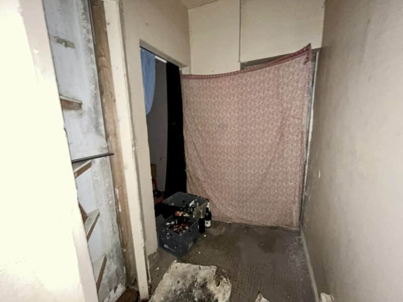 Rear room at 2307 E. Preston Street with worn carpeting, exposed wood, and miscellaneous debris