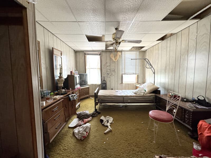 First bedroom of 3412 Esther Place featuring vintage decor, drop ceiling, and clutter—showcasing opportunity for full renovation.