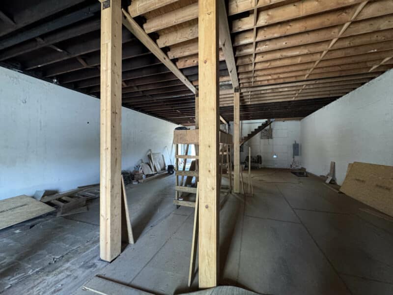 Interior shot of unfinished commercial space with open framing, exposed ceiling joists, and plywood flooring.